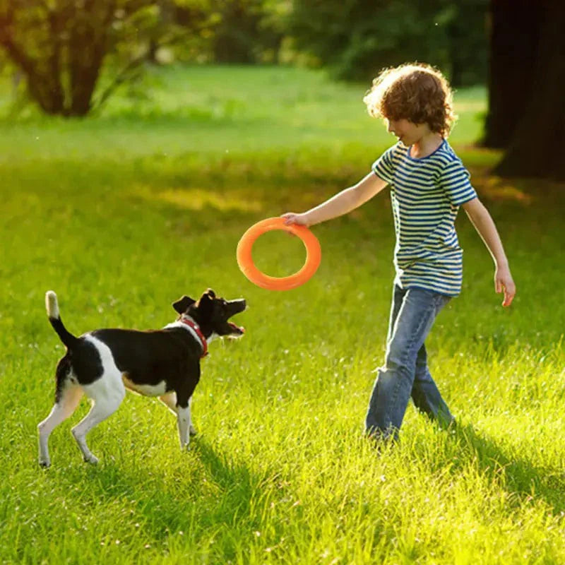 Child playing with dog using an orange EVA Pull Play Ring in a grassy park